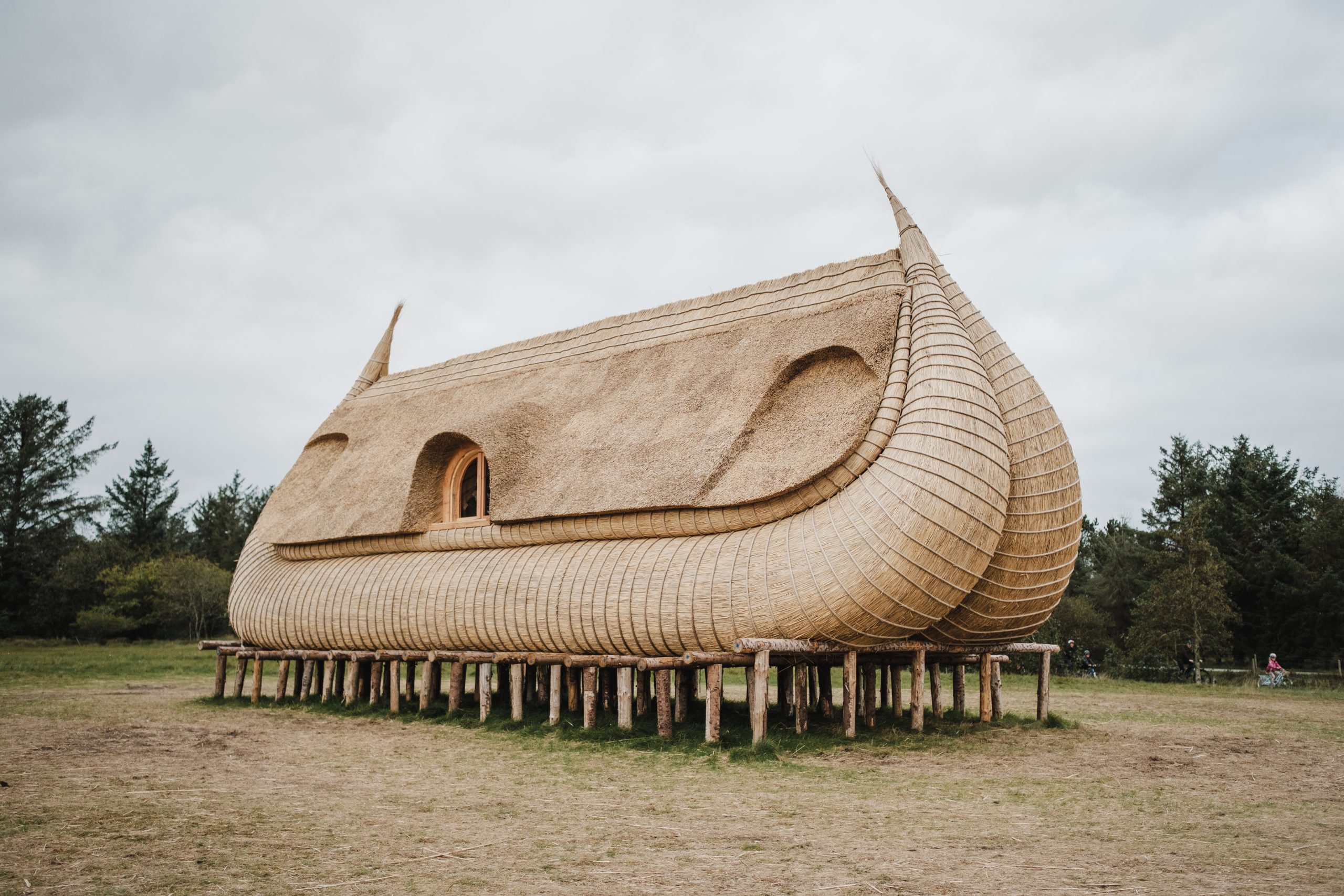 The houseboat is outside in a clearing surrounded by trees, supported by wooden plinths