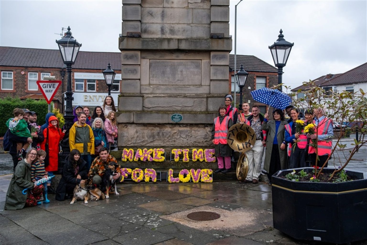a group of people stand either side of a stone structure. The wear raincaots and hold umbrellas