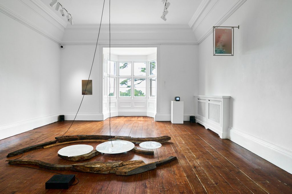 Gallery installation shot. Three white disks hover above pieces of drift wood