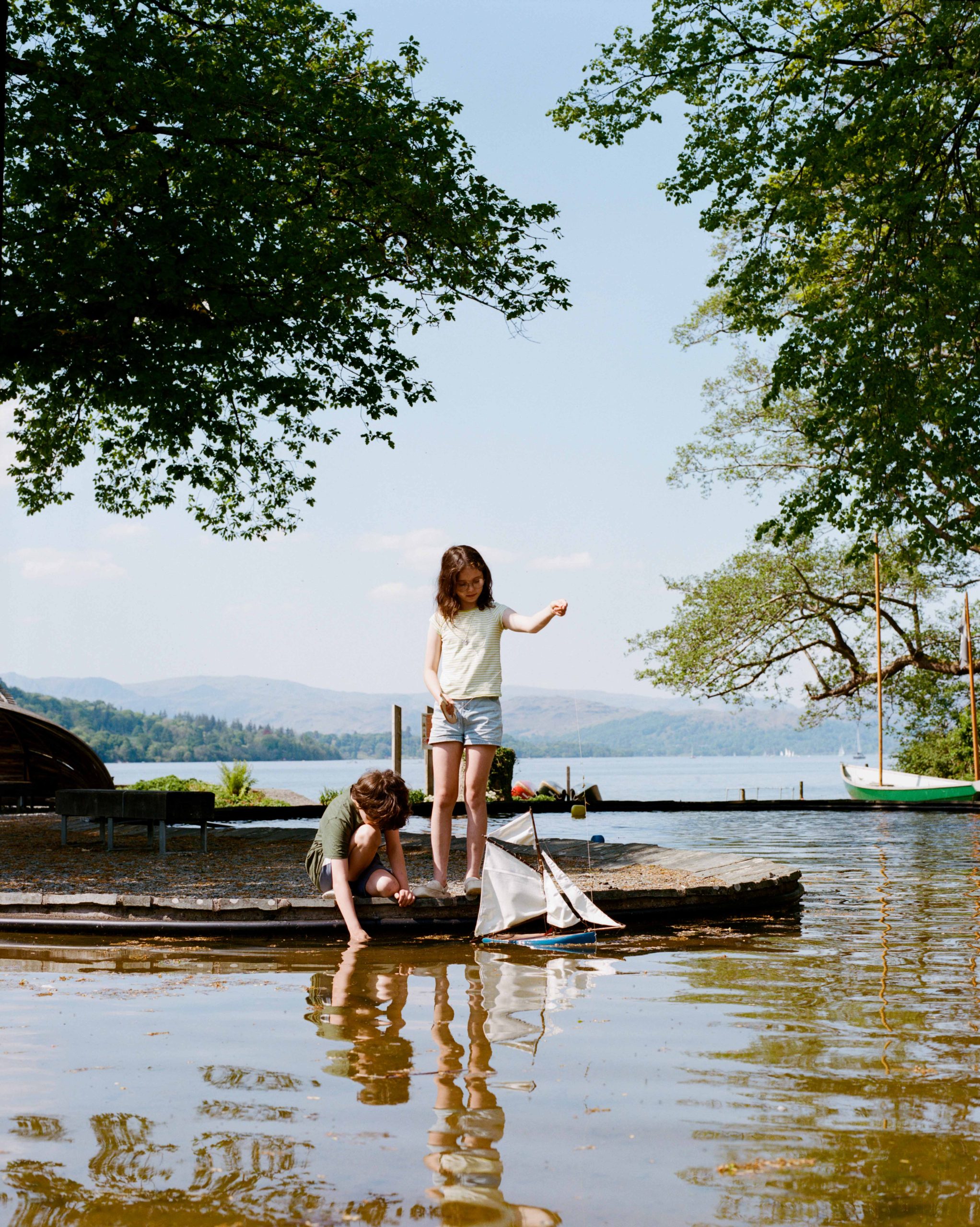 Two small white children play in the water with a toy boat