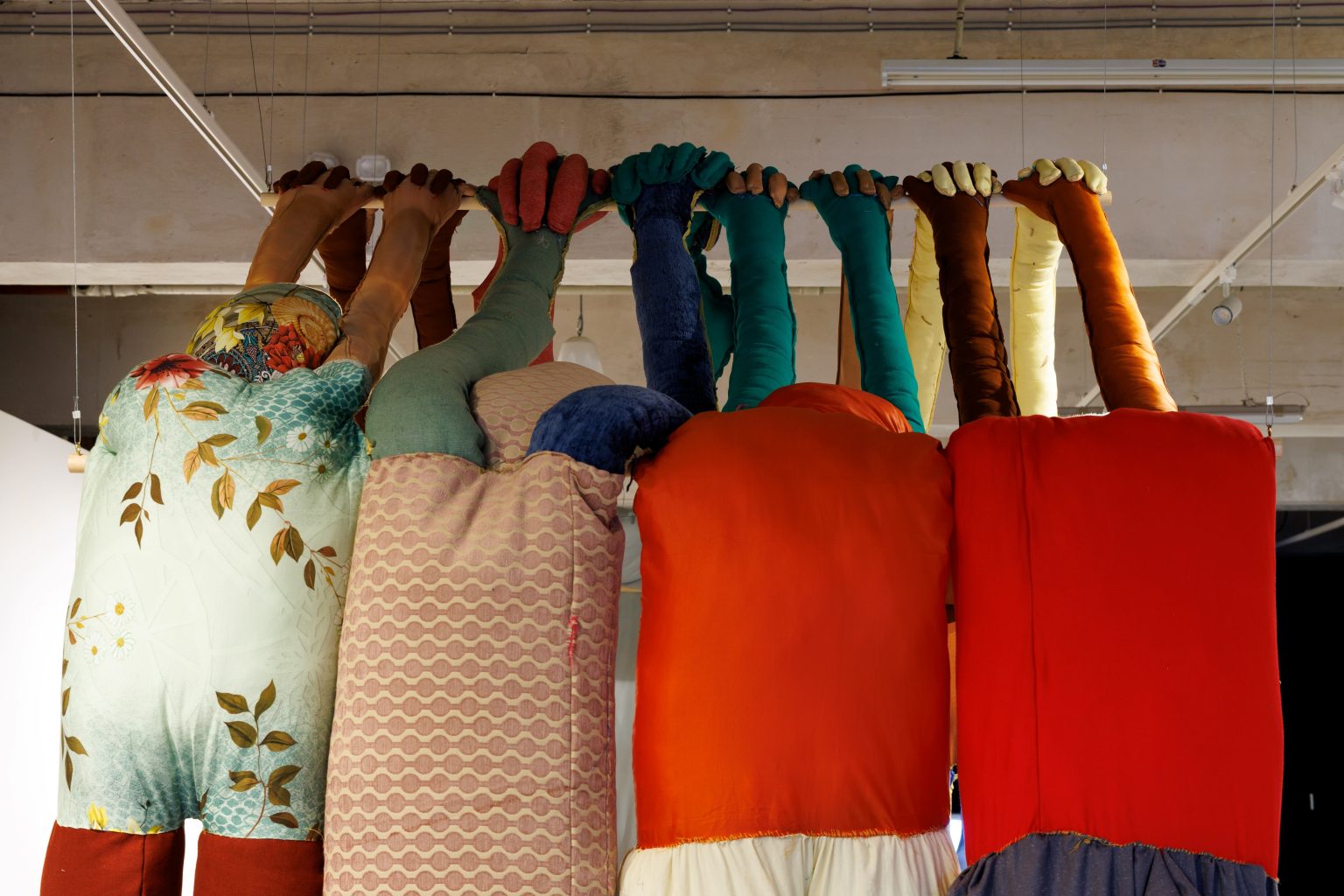 A row of the backs of several large colourful ragdolls with their arms outstretched, forming an arch with a row of ragdolls opposite.