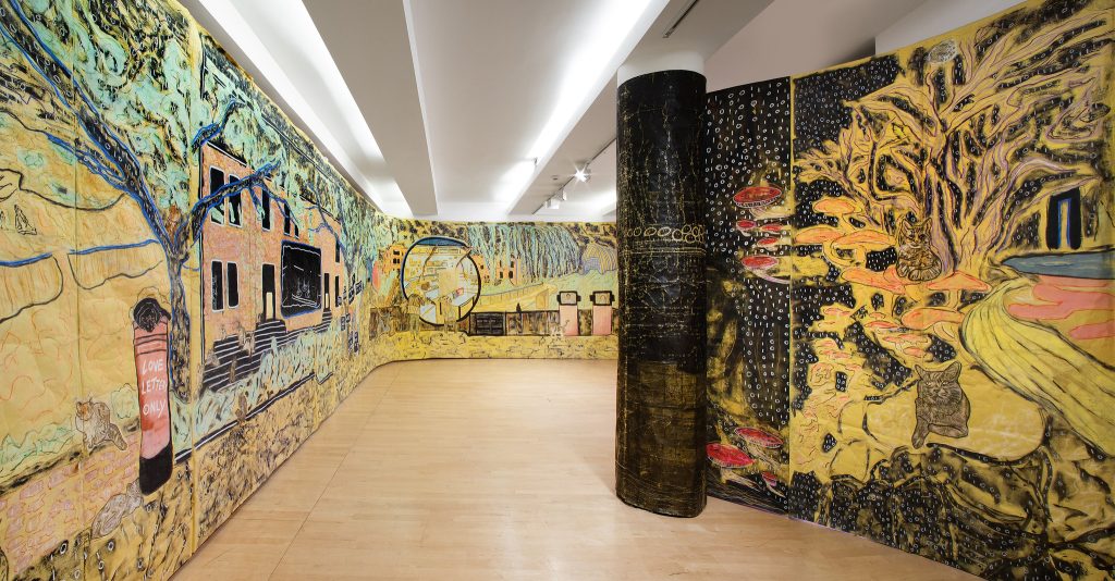 A walkway between huge floor to ceiling drawings on paper showing plants and animals and buildings