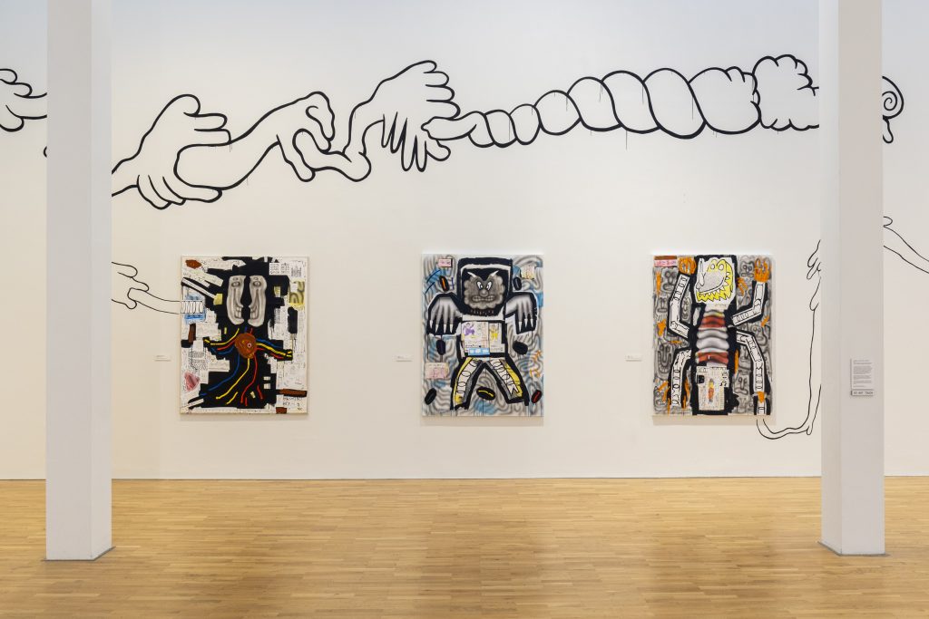 3 large colourful paintings installed on the back wall of the gallery are intersected with a giant black wall painting