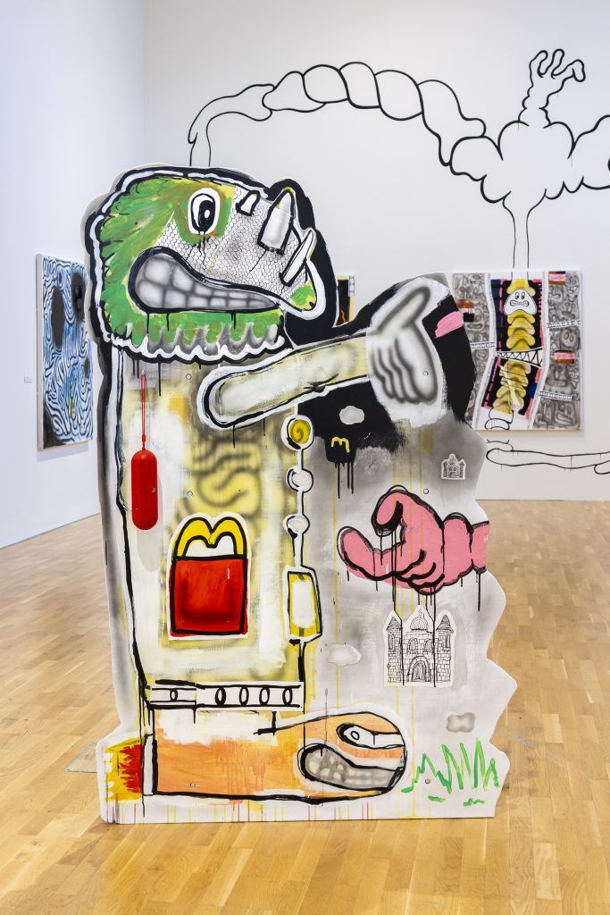 A multi-coloured wooden cutout is painted with cartoonish characters and symbols - part of a bigger installation