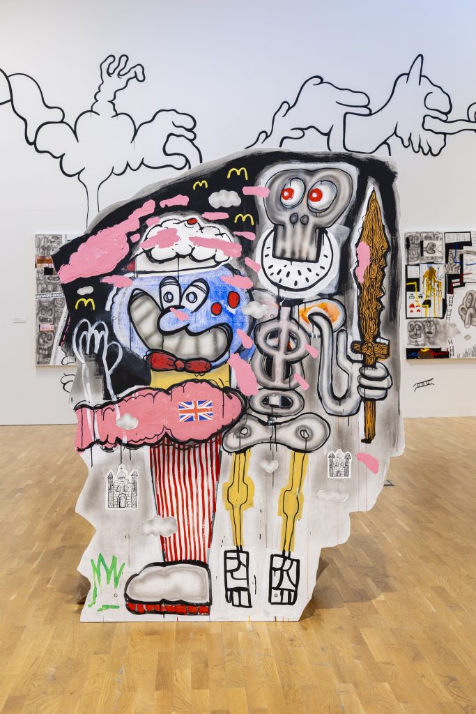 A multi-coloured wooden cutout is painted with cartoonish characters and symbols - part of a bigger installation