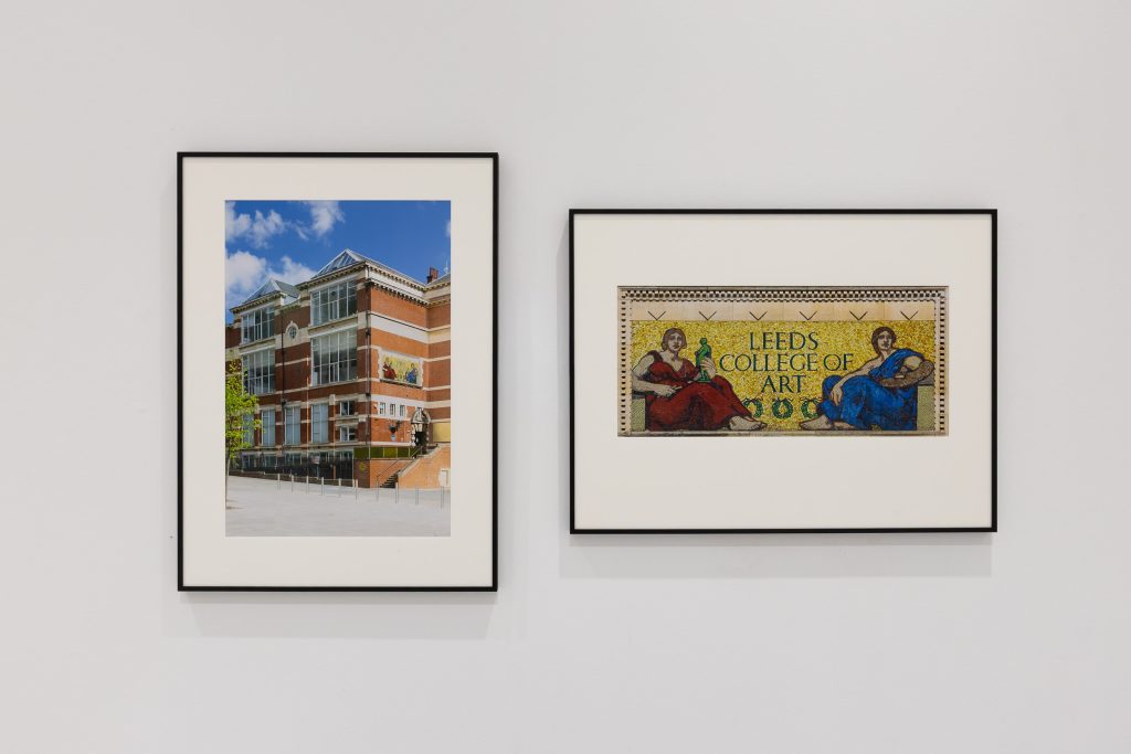 Two framed images on a white wall. One is a photo of the Leeds Art University building, the second is an image of a mural that reads Leeds College of Art and has two classical figures, probably the muses of music and painting.