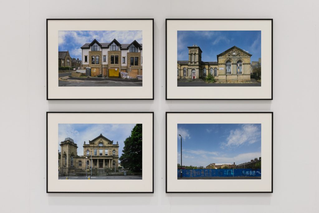 Four framed, large format photos of buildings displayed on a white wall.