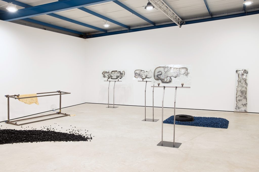 Wide view of the gallery with glass panel works on metal stands and black rubber across the floor