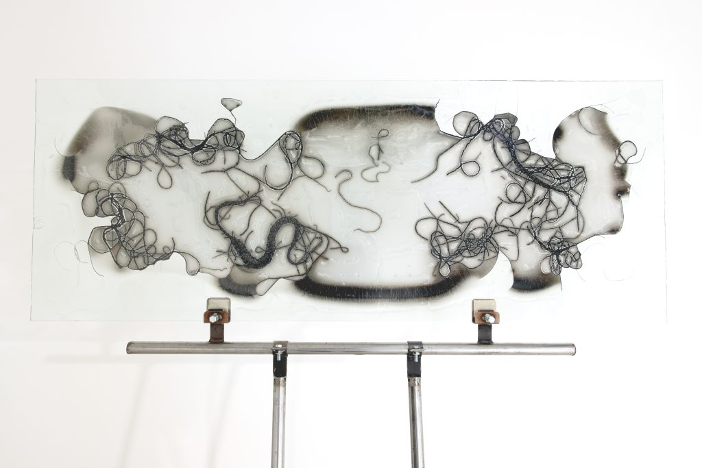 A hazy glass panel with black strands fused into it like wiggly worms is held up by clean silver metal poles