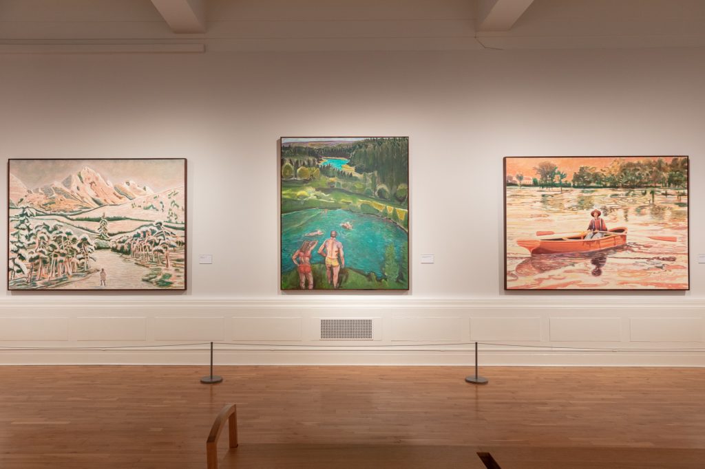 Three landscape paintings on a gallery wall: left, a winter mountain scene with small figures in the foreground; centre, two people poised as if to jump into a river in summer; a person in a boat on a river