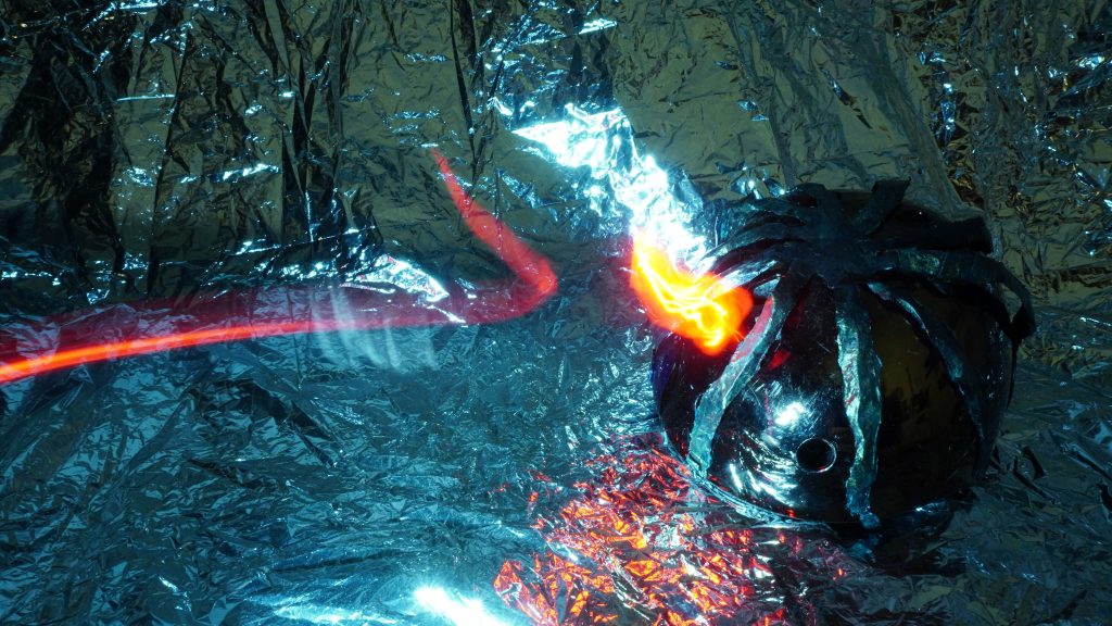 A strange helmet-like object on a silver ground, coloured lights dragging over the surface