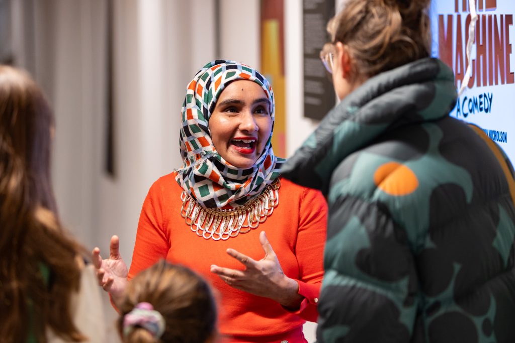 A person in colourful clothing and a headscarf talks animatedly to two other people