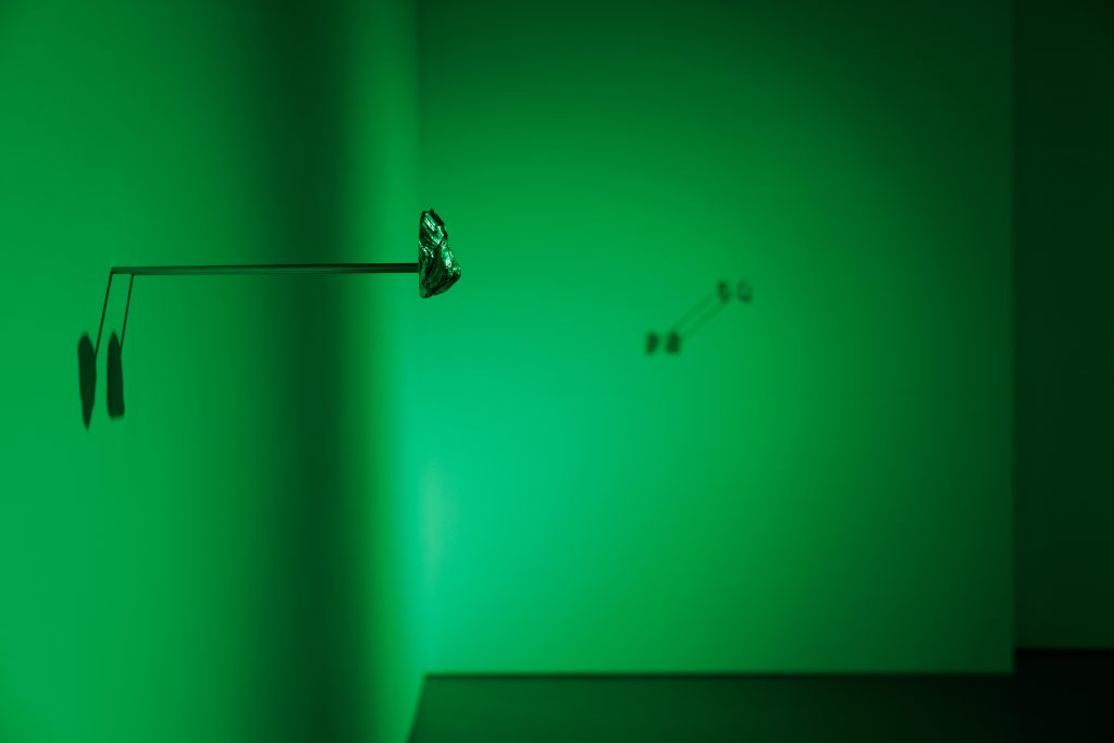 Small metallic sculptures juts out of the wall about 1ft, lit in fluorescent green light