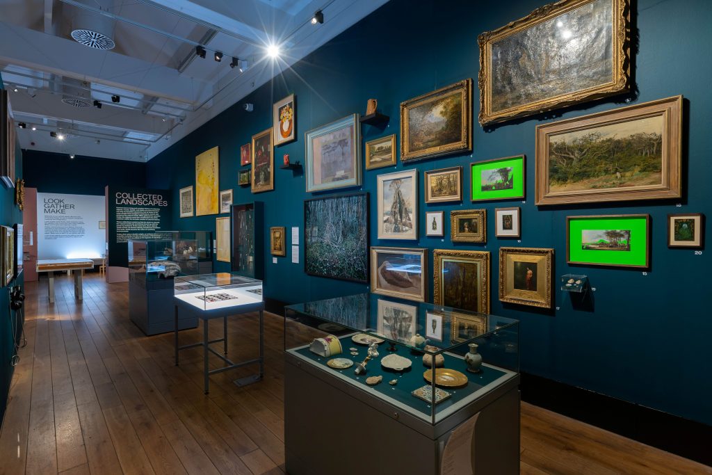 A museum gallery with dark blue walls, densely packed with framed paintings and vitrines filled with a variety of objects