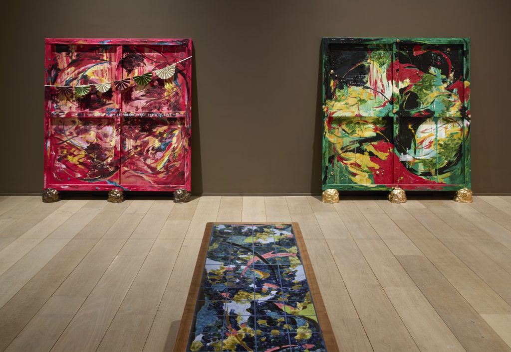 Two large abstract paintings on the backs of canvases with the crossed wooden support visible in the painting, on the left pinks and reds and on the right greens and blacks, with a view of one of the tops of the tiled benches in front, with pink, blue and white paint