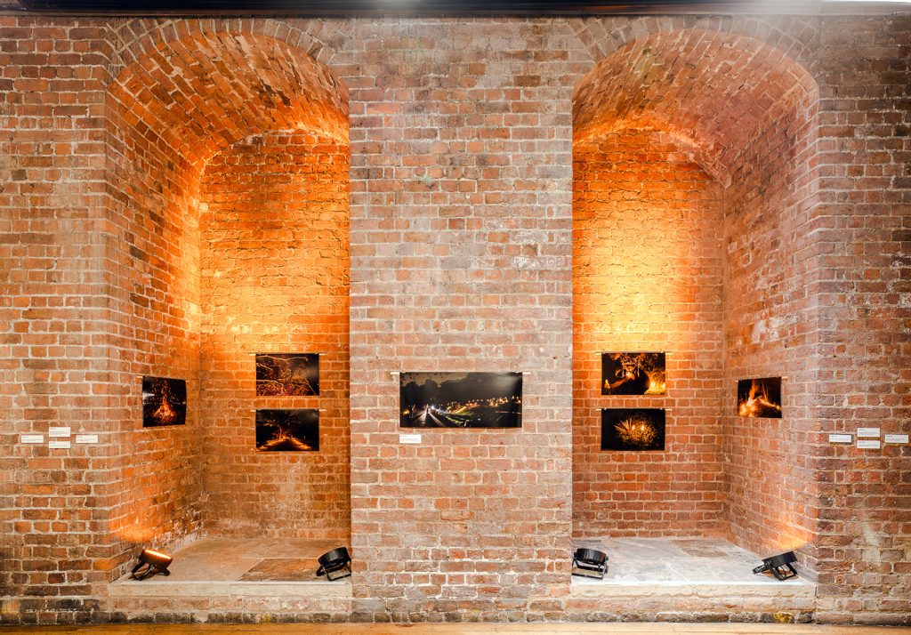 Installation shot. Photographs of a cemetery at night are hung inside a pair of red brick alcoves. 