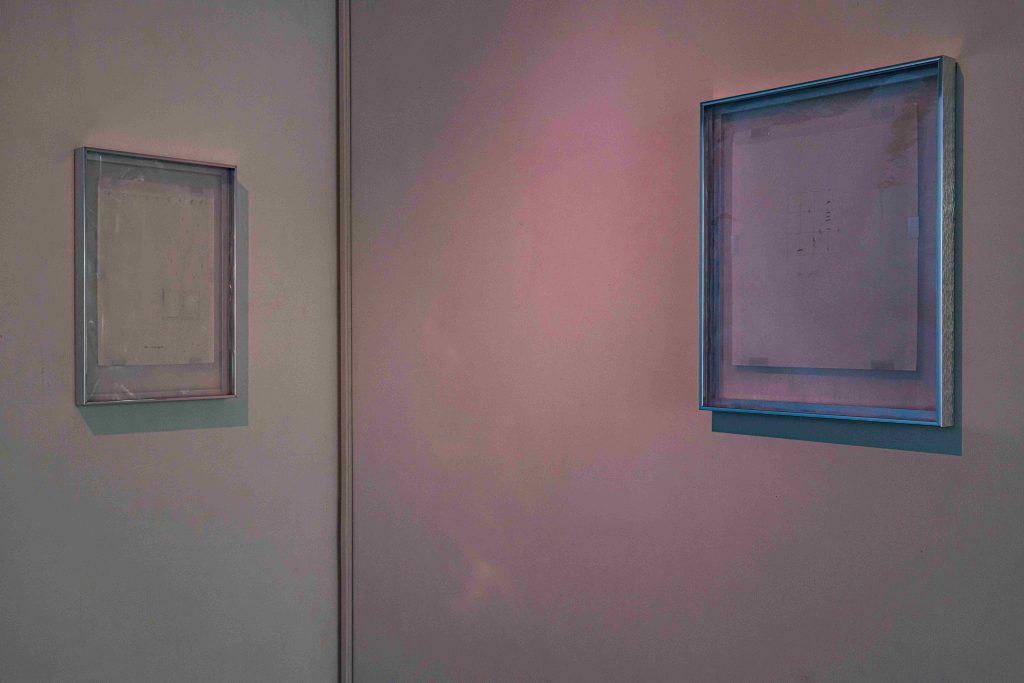 Two framed drawings in the corner of a room bathed in pink light