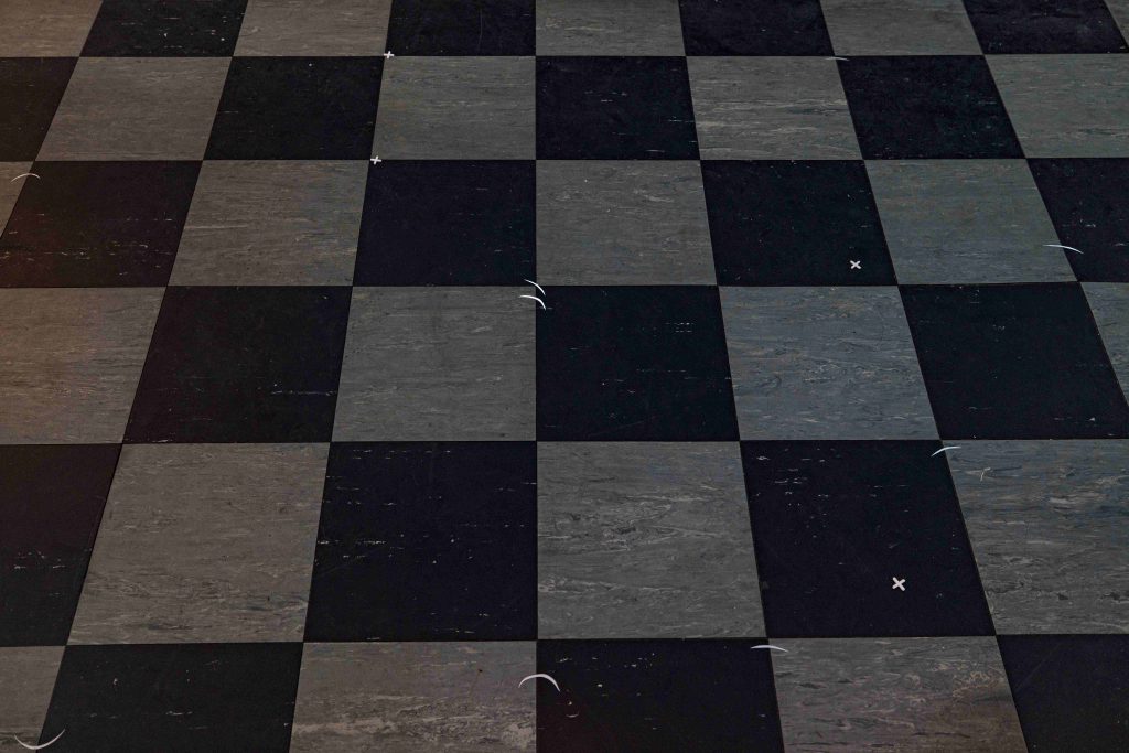A black and white checked lino floor with small white crosses and crescent slivers of white paper