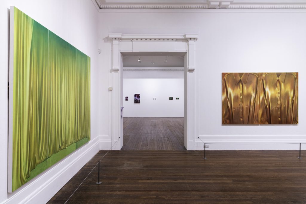 Two luminous paintings, on the left golden chartreuse drapes fill the whole image with green shading and on the right two bronze shirts reflect back golden light