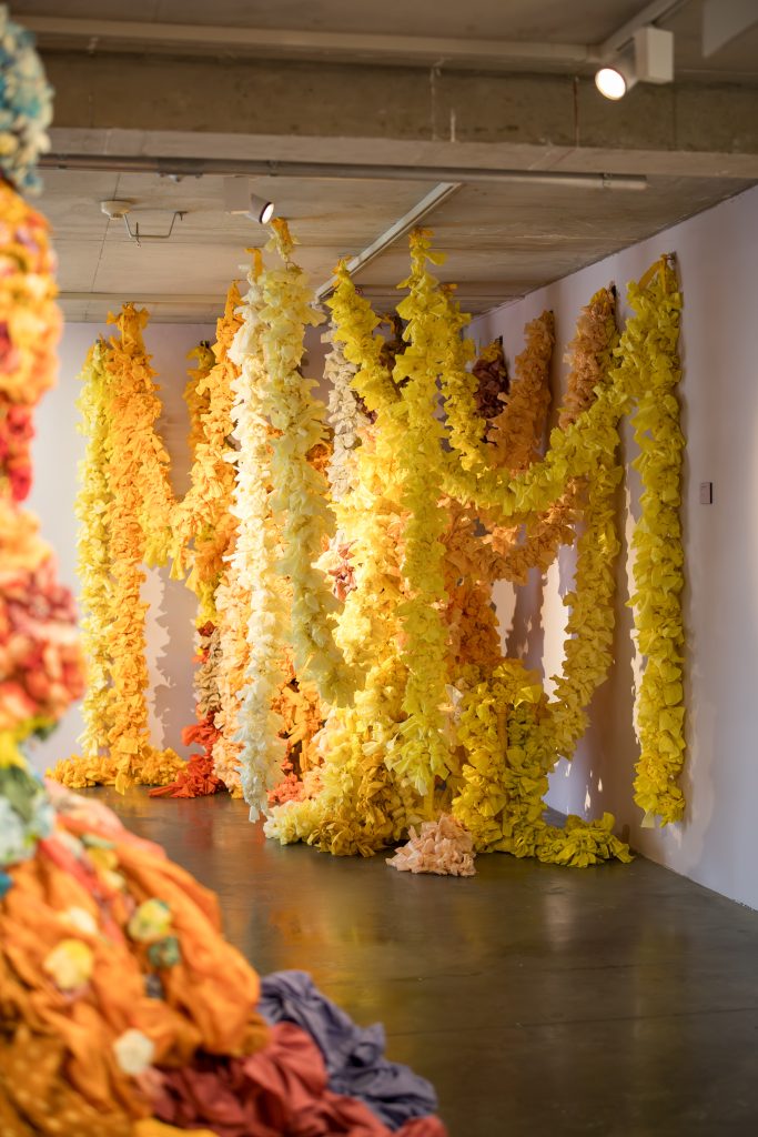 A corner installation of large garlands made of yellow fabric in different hues, gathered together to occupy the space.