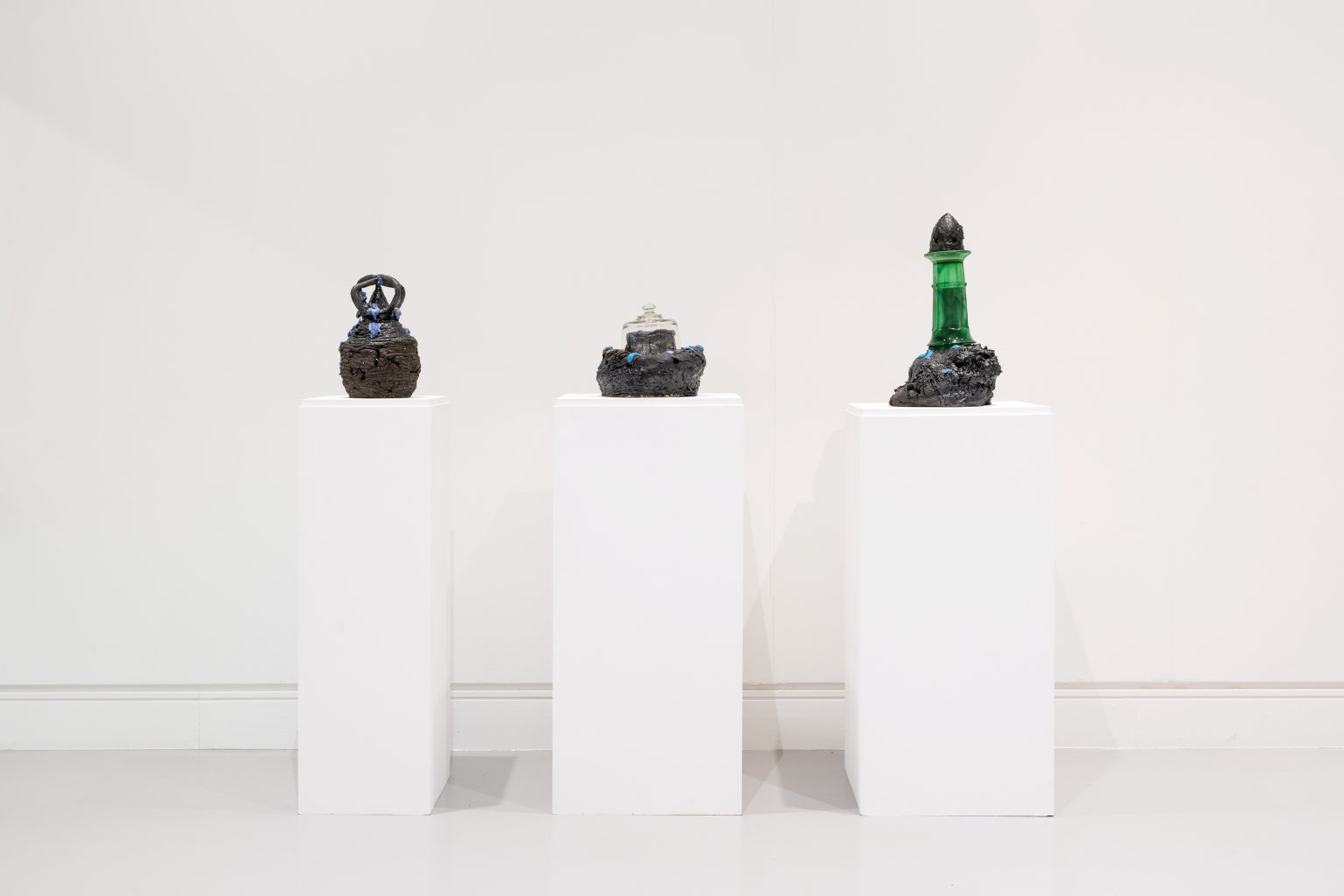 Three dark ceramic forms on tall, slender plinths