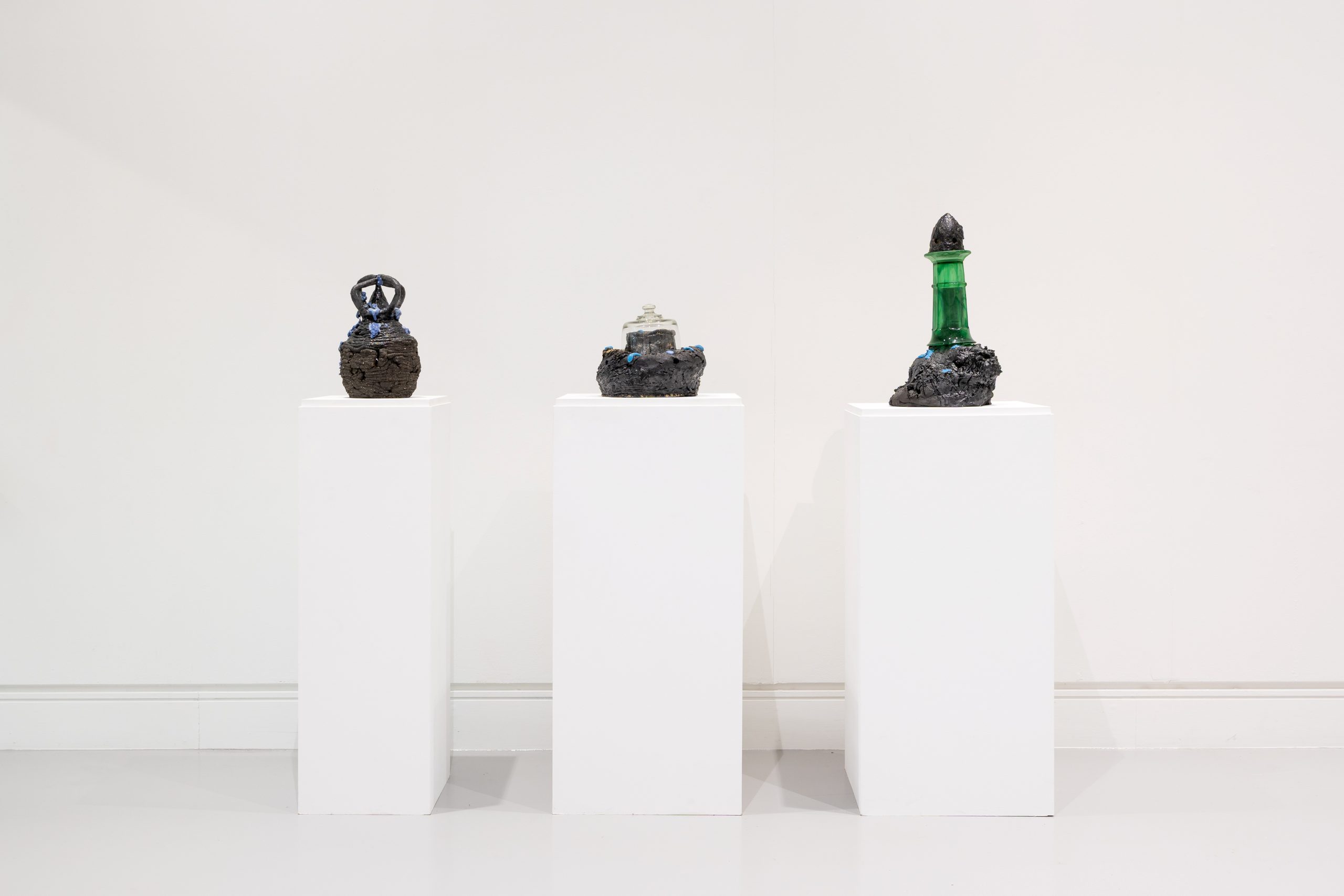 Three dark ceramic forms on tall, slender plinths