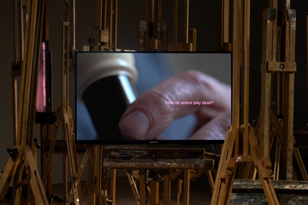film still. a close up of an elderly looking hand playing the recorder. the text across the image reads 'How do actors play dead?'.