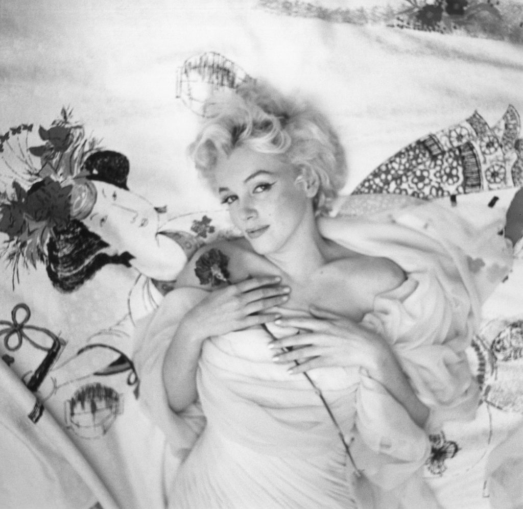 An iconic image of Marilyn Monroe, dressed in white, reclining on a bed and holding a red rose to her face