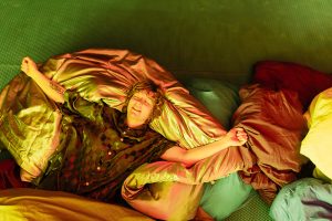 A person lies on a pile of duvets, arms outstretched a look of happy relaxation on their face.