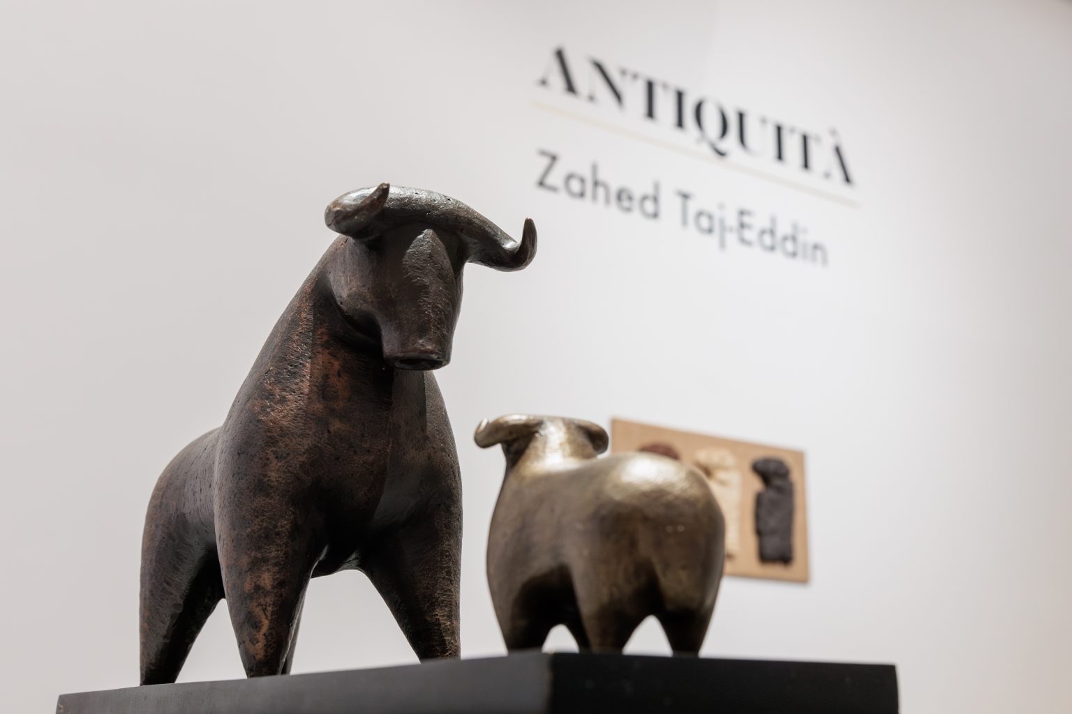 a bronze sculpture depicting a bull towering over a sheep. both animals face each other head on.