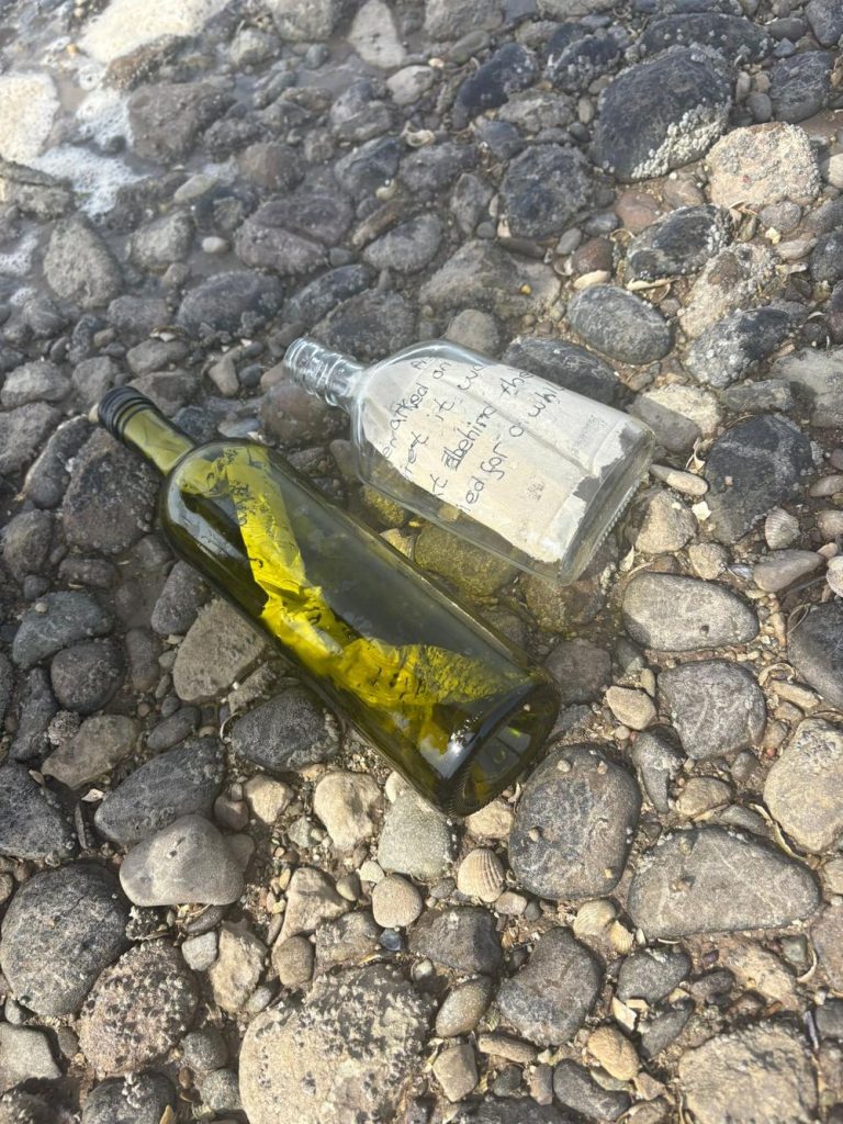 Two glass bottles on a pebble beach with handwritten messages on paper twisted inside