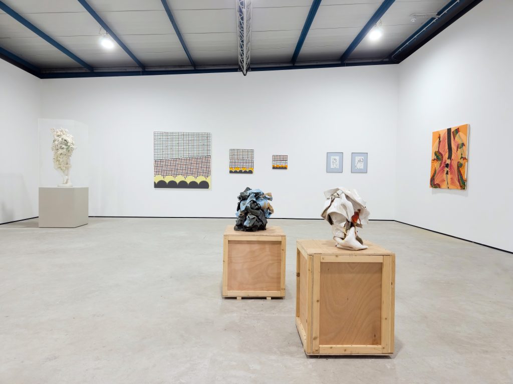 A wide view of the gallery with two bare wood plinths in the foreground carrying sculptures of scrunched up pieces of paper