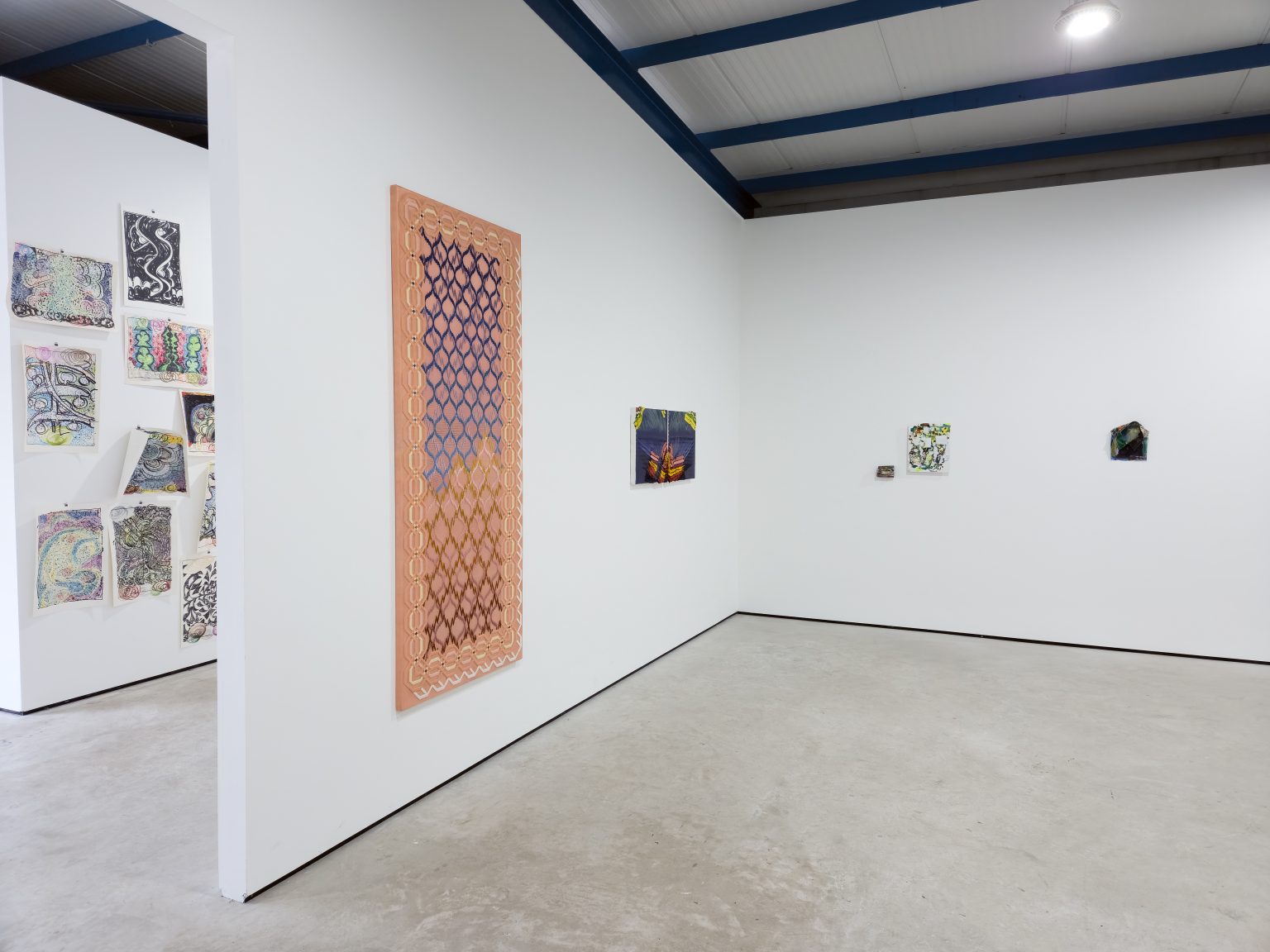 White walled gallery with wall mounted paintings, in the foreground a crisscrossed painting of dark blue and red lines on a peach background