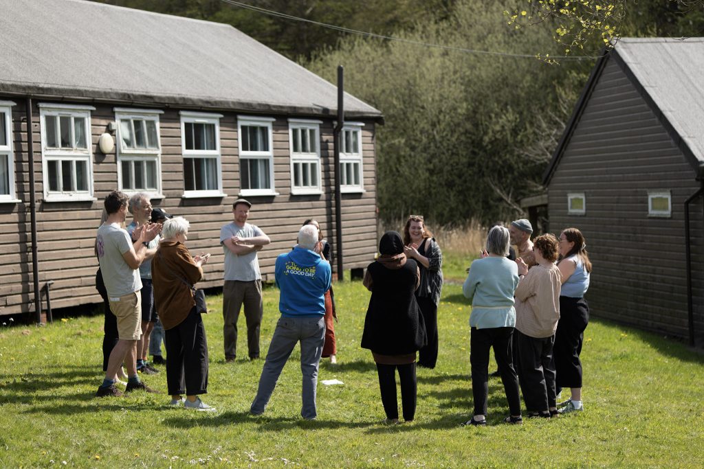 A group of people outside standing in a circle all smiling and clapping