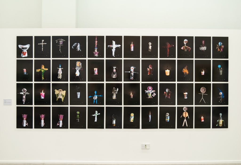 A wall of black background photographs with small totemic figurines on them