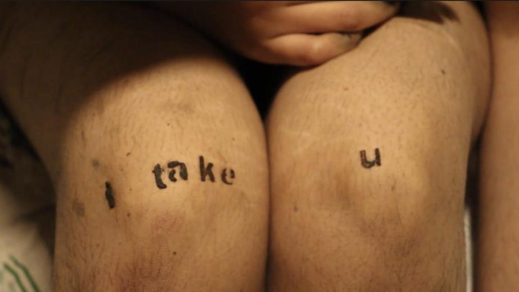 A pair of knees printed or tattooed with the words 'i take // u'