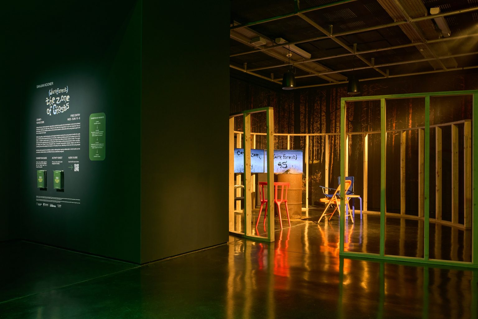 A dark room with a circular wooden frame in the centre, in which are two chairs and a TV screen.