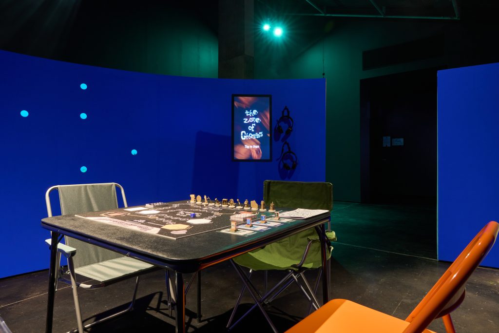 A board game sits on top a black table, surrounded by a royal blue wall and two vacant chairs .