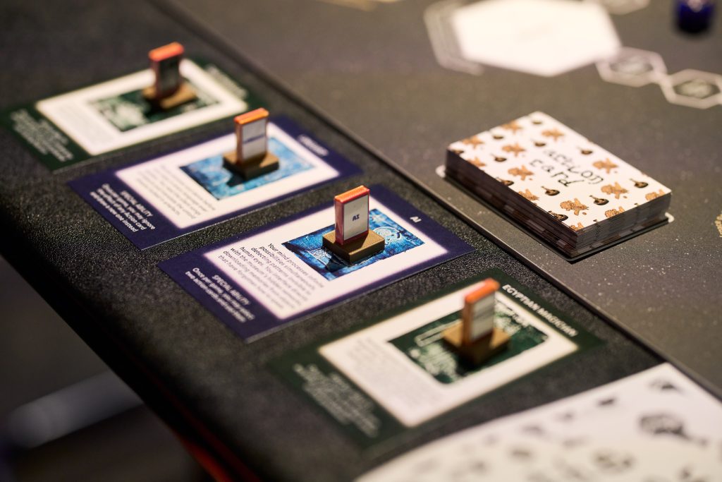 A detail of a board game with cards featuring unclear images and text. Small playing pieces sit on top of the cards. 