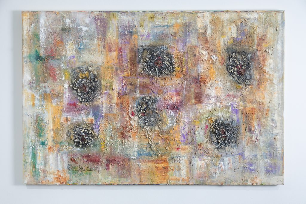 Installation view of one of Oliver Benoit's paintings in Roots Through Ruins at Coreset, Newark. The painting has a pale off white background with layers of different colours in green, purple and ochre hues. The texture of the paint is very rough in places suggesting that other matter has been worked into the paint.
