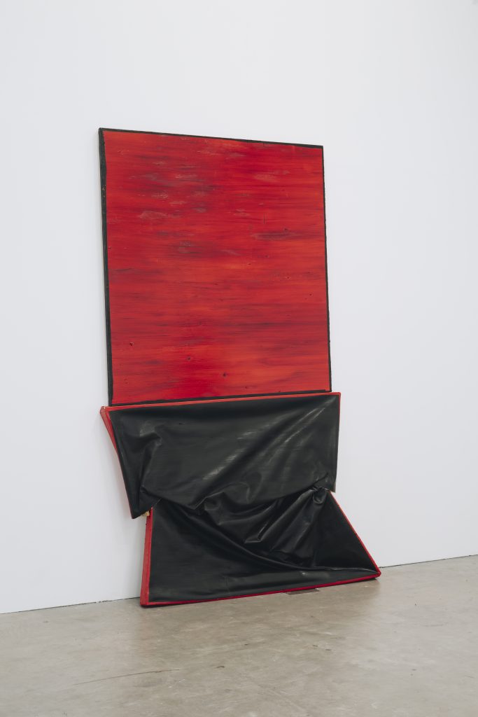 An off-square red painting sits on top of a similar sized black painting, which is squashed, and pushed to the floor by the painting above it.