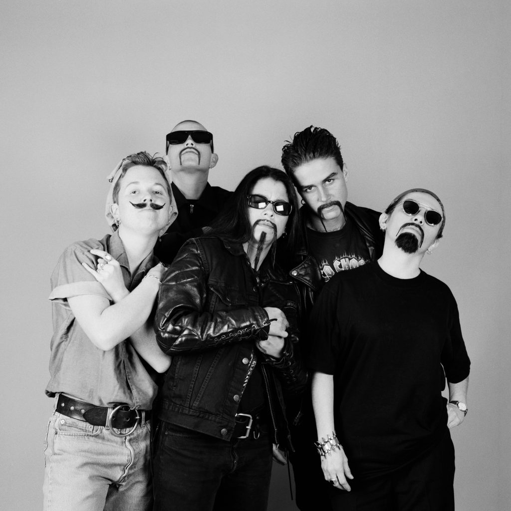 a group of butch looking females pose together as if they are in a metal band. They each wear a fake moustache