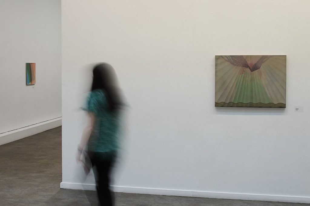 A blurred figure moves past a mystical painting of lines of light fanning out from a sky point
