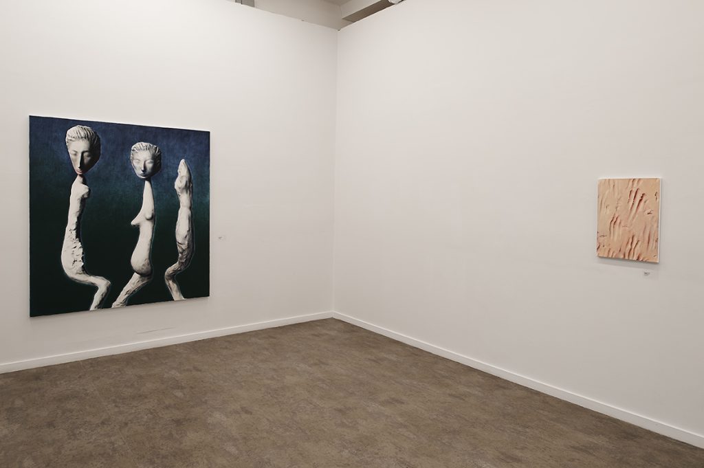 Three chiaroscuro figurines with alien faces and stretched out bodies in a square canvas to the left, on the right a small square like sand with handprints