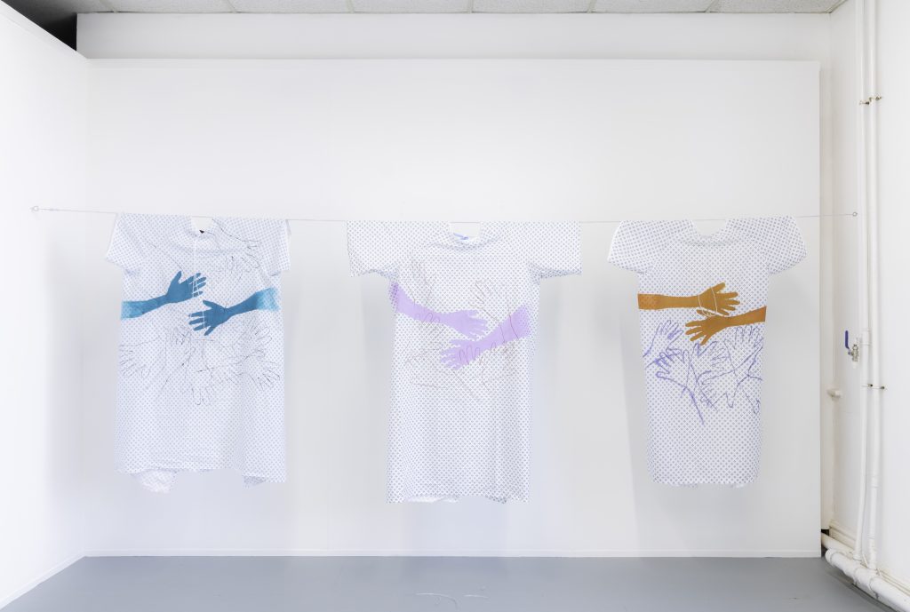 A washing line with three hospital gowns hung in a line with images of hands reaching out to each other on them