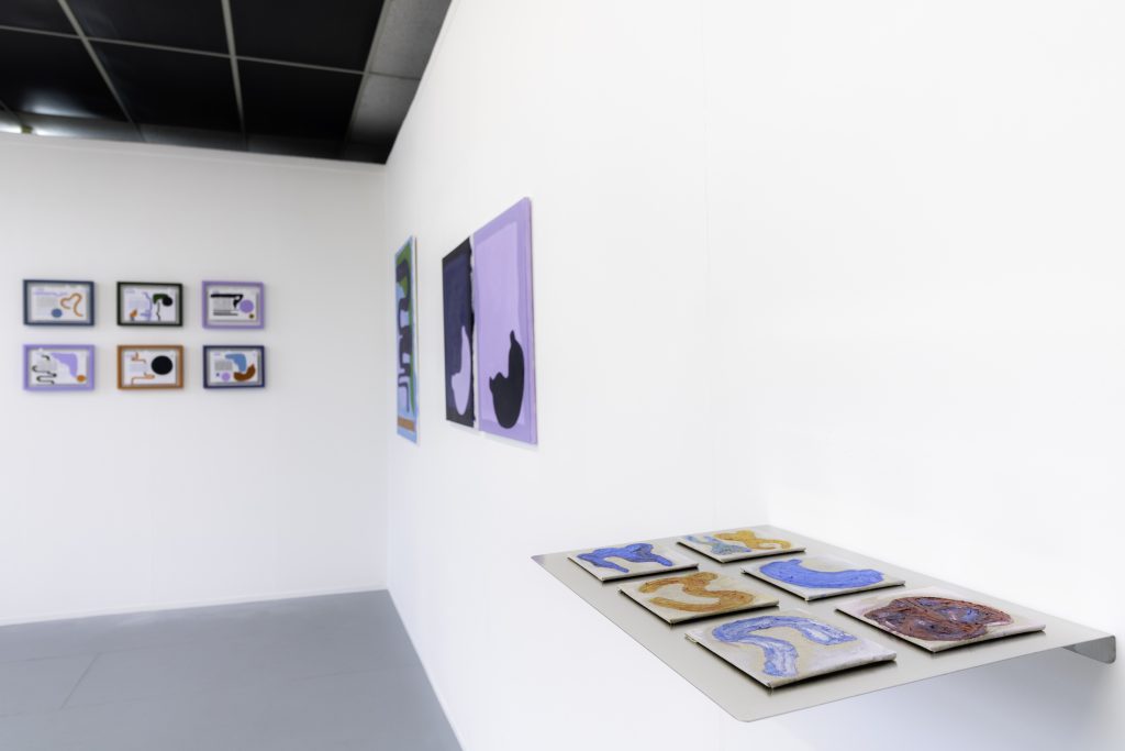 A waist high shelf with 6 flat bright abstract paintings