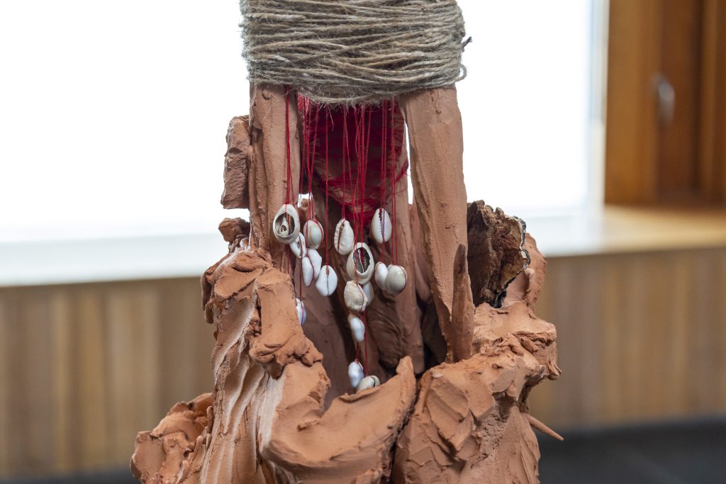 A close-up shot of a sculpture made from raw/natural materials like unfired clay, shells and twine