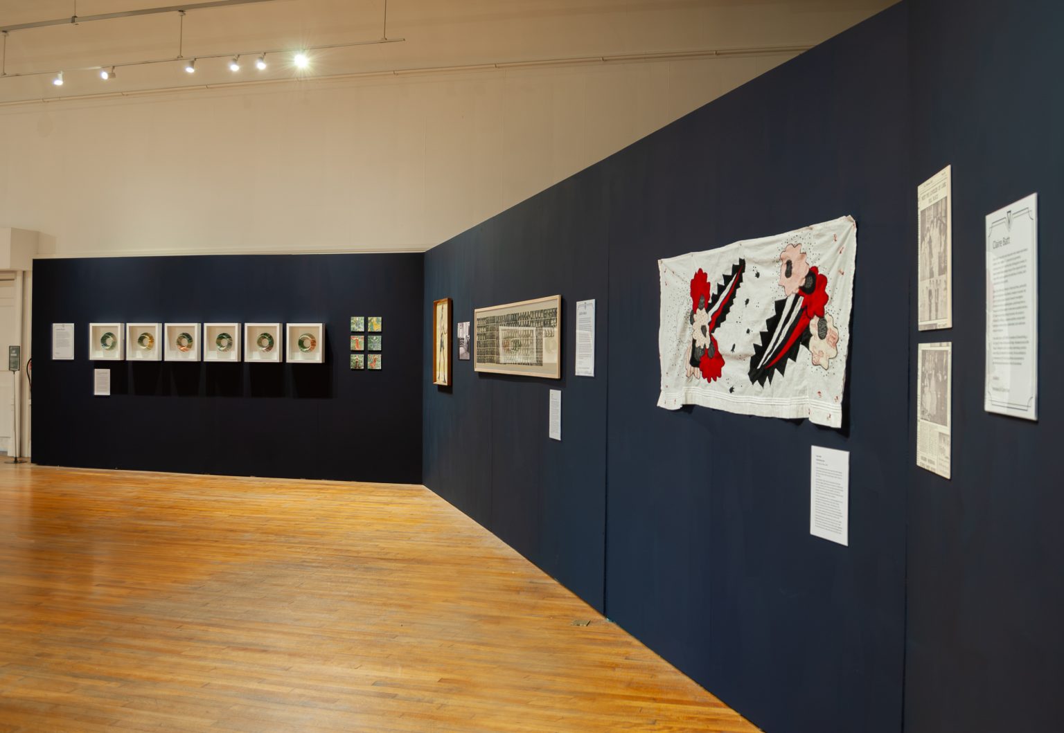 A dark gallery wall with light and white artworks hung in a straight line
