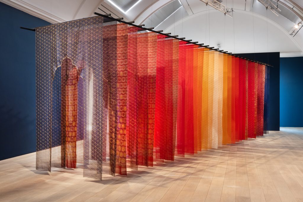 A bright corridor of luminous fabrics in reds and oranges with a doorway cut through to enter