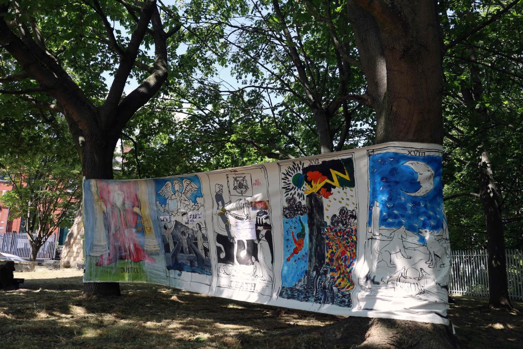 Colourful painted banners stretched between trees in a small park at the height of summer